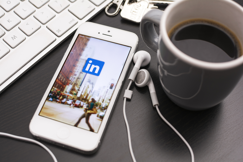 Linkedin logo on a phone with earphones, cup of coffee, and keys
